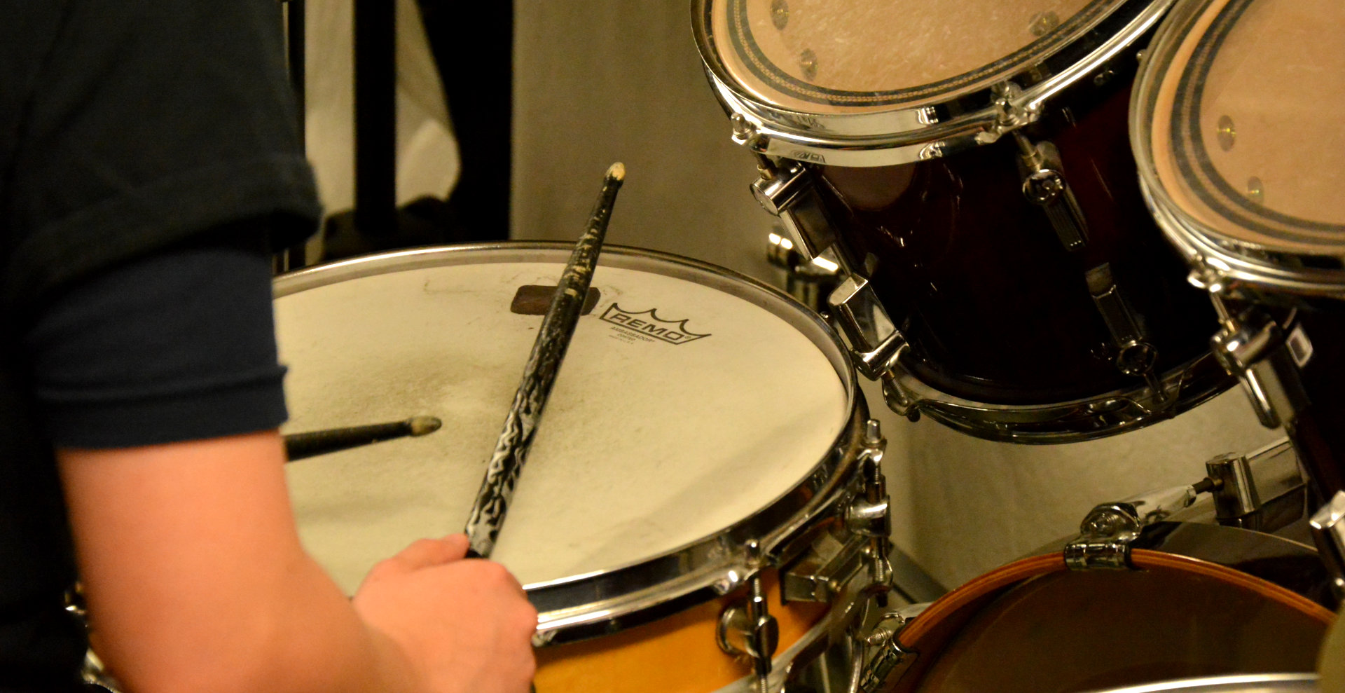 Drum stick over snare drum - background image for page heading. Contact Us at The Beat Studios.